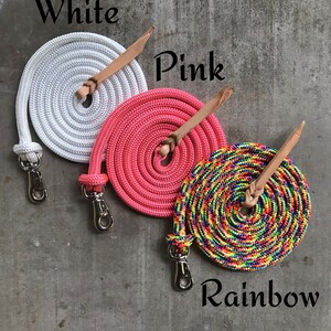 May include: Three coiled ropes with leather handles and metal clips. The ropes are white, pink, and rainbow.