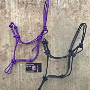 May include: Two horse halters, one purple and one black, made of rope with knots. The halters are hanging on a textured grey wall. A business card for "Tightrope Custom Tack" is visible in the bottom left corner.