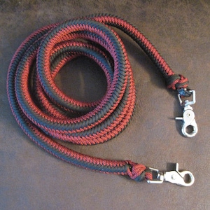 Puede incluir: Una correa de cuerda trenzada negra y roja con dos clips giratorios plateados.