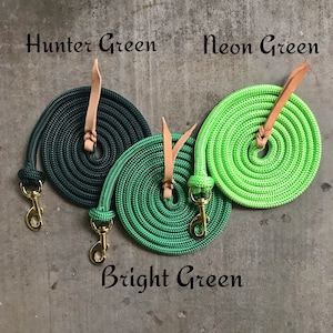 Op de afbeelding: Drie opgerolde touwen met leren banden en gouden gespen. De touwen zijn jagergroen, heldergroen en neon groen.