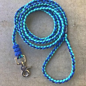 May include: A blue and teal braided dog leash with a silver clip. The leash is made of paracord and has a braided design. The leash is about 4 feet long.