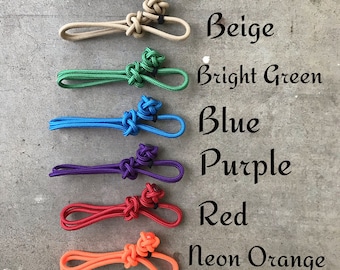Op de afbeelding: Een set van acht kleurrijke koorden met knopen aan de uiteinden. De koorden zijn zwart, beige, felgroen, blauw, paars, rood, neonoranje en neongroen.
