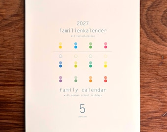 May include: A 2027 wall calendar with white pages and a silver wire spiral binding. The cover features the text 2027 familienkalender mit ferienterminen, family calendar with german school holidays, and 5 persons, along with a grid of colorful dots.