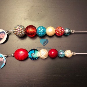 以下が含まれることがあります： 赤、白、青のビーズが付いたモアナをテーマにしたチャームブレスレット2本。各ブレスレットには、モアナの絵が描かれたチャームが付いています。