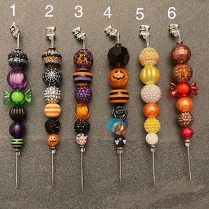 以下が含まれることがあります： ハロウィンをテーマにしたビーズキーホルダーが6つ。かぼちゃ、キャンディーコーン、クモなど、さまざまなデザインがあります。各キーホルダーは、シルバーの金属ループとシルバーの金属ピンに取り付けられています。