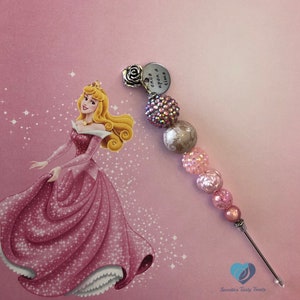 以下が含まれることがあります： ピンクと白のビーズチャーム。シルバーチャームには「Once upon a dream」の文字が刻まれています。ローズチャームも付いています。チャームは、ピンクの背景に眠れる森の美女のアニメーション画像が描かれています。
