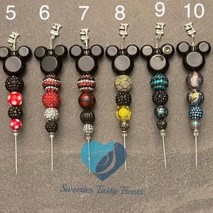 以下が含まれることがあります： 14個の装飾的なボトルストッパーのコレクション。各ストッパーは、黒いミッキーマウスの頭のデザインと、さまざまなカラフルなビーズが特徴です。ストッパーは灰色の背景に並んで配置されています。「Sweeties Tasty Treats」というテキストが表示されます。