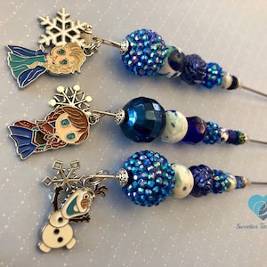 以下が含まれることがあります： 3本の青と白のビーズ付きかき混ぜ棒。それぞれに金属製のチャームが付いています。チャームは映画アナと雪の女王のキャラクターで、エルサ、アナ、オラフがいます。
