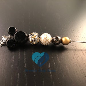 以下が含まれることがあります： ミッキーマウスのヘッドチャーム、クリアなラインストーンビーズ、幾何学模様の白いビーズ、レース模様の黒いビーズ、金色のビーズが付いた黒と金のビーズチャームブレスレットです。