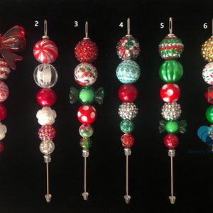 以下が含まれることがあります： 6つのクリスマスオーナメントピックのコレクション。各ピックは、赤、白、緑、金色の様々な装飾ビーズが特徴です。一部のピックには、リボンやキャンディー型のビーズが付いています。これらのピックは、休日の装飾用に設計されています。