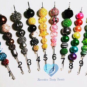 以下が含まれることがあります： 異なるデザインと色のカラフルなビーズキーホルダーが10個。各キーホルダーにはシルバーの金属フックが付いており、1から10まで番号が付けられています。