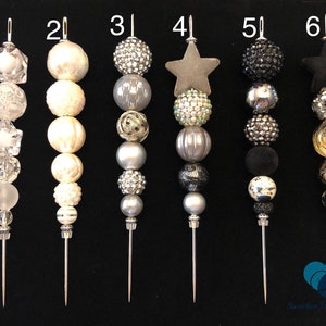 以下が含まれることがあります： 星、クリスタル、ビーズなどのさまざまな装飾が施された、銀と黒のビーズのスティックピンが6本あります。ピンは1から6まで番号が付けられています。