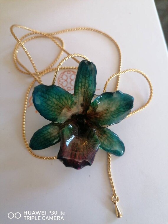 Natural green/purple orchid with yellow reflections incorporated in resin with galvanized gold latches adjustable as desired