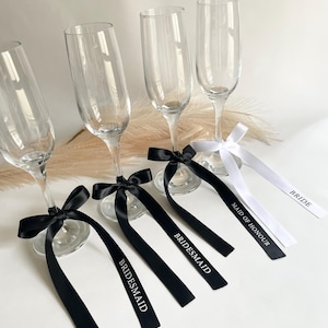 Pu&ograve; includere: Quattro calici di champagne con nastri neri e bianchi. I nastri neri sono legati con fiocchi attorno alla base dei calici e hanno la parola "Bridesmaid" stampata. Il nastro bianco ha le parole "Maid of Honour" e "Bride".