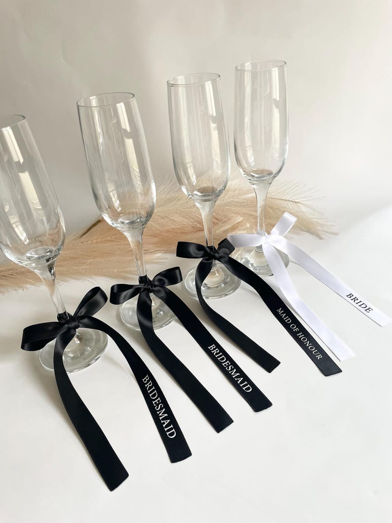 Pu&ograve; includere: Quattro calici di champagne con nastri neri e bianchi. I nastri neri sono legati con fiocchi attorno alla base dei calici e hanno la parola "Bridesmaid" stampata. Il nastro bianco ha le parole "Maid of Honour" e "Bride".