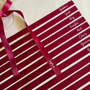 Pu&ograve; includere: Segnaposto bordeaux con nomi bianchi, come Sophie e Josh. Un nastro bordeaux abbinato &egrave; legato a fiocco. Le carte sono disposte in diagonale, perfette per un matrimonio o un evento.