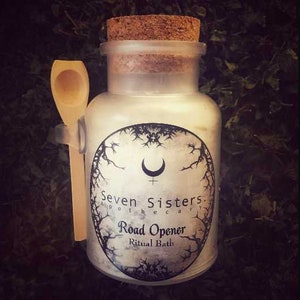 Puede incluir: Un frasco de vidrio con tapa de corcho lleno de sales de baño blancas. El frasco tiene una etiqueta en blanco y negro que dice "Seven Sisters Apothecary Road Opener Ritual Bath".