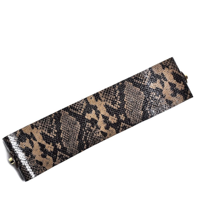 May include: A brown and black snakeskin patterned leather bracelet with gold-toned hardware.