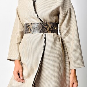 May include: A beige striped wrap coat with a black zipper detail and a brown and black snakeskin belt.