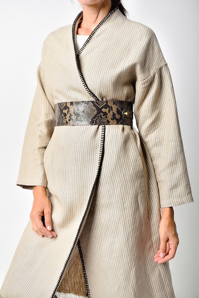 May include: A beige striped wrap coat with a black zipper detail and a brown and black snakeskin belt.