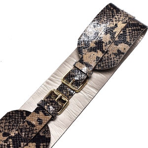 May include: A wide brown and black snakeskin belt with gold-toned buckles. The belt is made of two layers of leather, with the top layer being a snakeskin pattern.