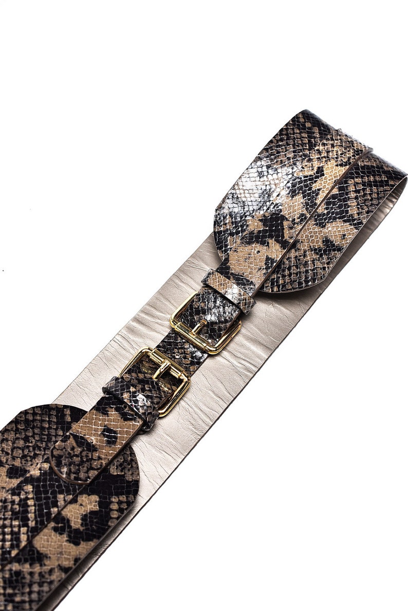 May include: A wide brown and black snakeskin belt with gold-toned buckles. The belt is made of two layers of leather, with the top layer being a snakeskin pattern.