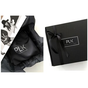May include: A black box with a white ribbon and the text "PLK Designer Leather Goods" on the front. The box is sitting on a black surface.