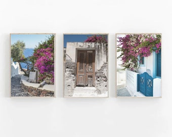 May include: Three framed prints of a Greek village with whitewashed walls, blue doors, and vibrant pink bougainvillea flowers. The prints feature a narrow cobblestone street, a weathered wooden door, and a close-up of the flowers.