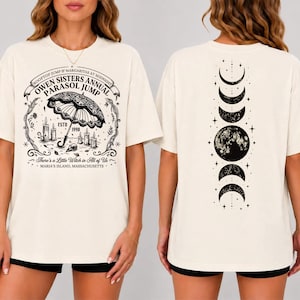 May include: An off-white t-shirt featuring black graphic prints. The front displays an umbrella, candles, and text reading "Owen Sisters Annual Parasol Jump". The back features a vertical sequence of moon phases and stars in black ink.