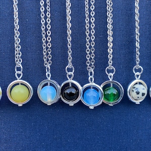 May include: A set of ten silver necklaces with a spinning orb pendant. Each orb is a different color, including purple, yellow, white, black, blue, green, white with black spots, black, and brown.