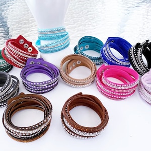 May include: Assortment of colourful wrap bracelets with rhinestones. Each bracelet is made of multiple layers of faux leather with a row of rhinestones on each layer. The bracelets are available in colours such as teal, purple, pink, brown, grey, and black.