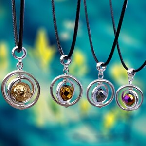 May include: Four silver necklaces with black cords and different colored gemstone pendants. Each pendant is a sphere encased in a silver ring.