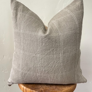 May include: A gray linen pillow with a white grid pattern. The pillow is sitting on a wooden stool.