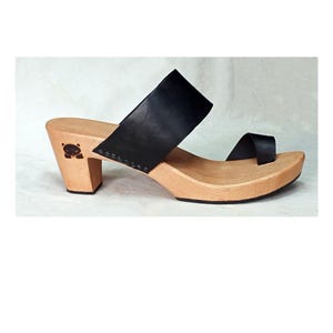 May include: Black leather heeled sandals with a wooden platform and a small black animal design on the heel.
