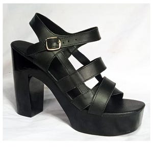 May include: Black platform sandals with a chunky heel. The sandals feature multiple straps across the foot and an ankle strap with a gold-colored buckle. The heel is approximately 4 inches high.