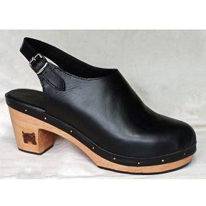 Puede incluir: Zueco de cuero negro con tacón de madera y correa de slingback. El tacón tiene un pequeño diseño tallado.