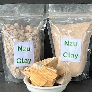 May include: Two bags of Nzu Clay, one with chunks of clay and one with powdered clay. A small white bowl holds a few larger pieces of clay.