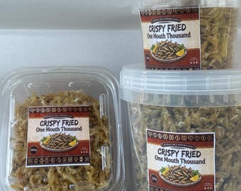 May include: Three clear plastic containers filled with small, dried, crispy fried fish. Each container features a label with the text "CRISPY FRIED One Mouth Thousand" and an illustration of a plate of fish. The containers are of varying sizes.
