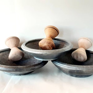 May include: Three dark gray mortar and pestle sets. Each set includes a round, shallow mortar with a textured interior and a wooden pestle. The pestles are light brown with a rounded top and a narrower middle section.