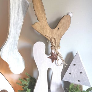 Op de afbeelding: Houten kerstversieringen. Een wit geschilderde kous, een rendier met een bruine kop en witte romp, en een witte kerstboom. Het rendier heeft een ster en touwdetails. De boom heeft steraccenten.