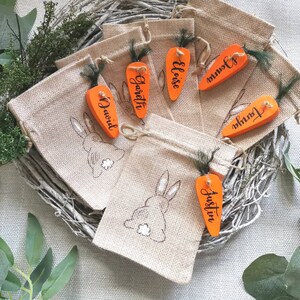 May include: Set of 6 burlap gift bags with carrot-shaped tags. The tags are decorated with the names "Garrett", "Eloise", "Justin", "David", "Tonia", and "Jowin".