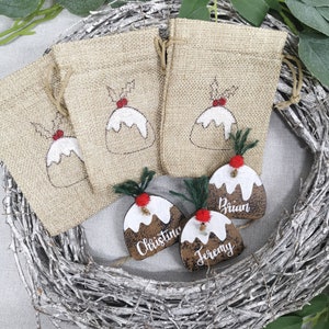 May include: Three brown wooden Christmas ornaments shaped like Christmas pudding with white icing and red holly berries. The ornaments are personalized with the names "Brian", "Christine", and "Jeremy".