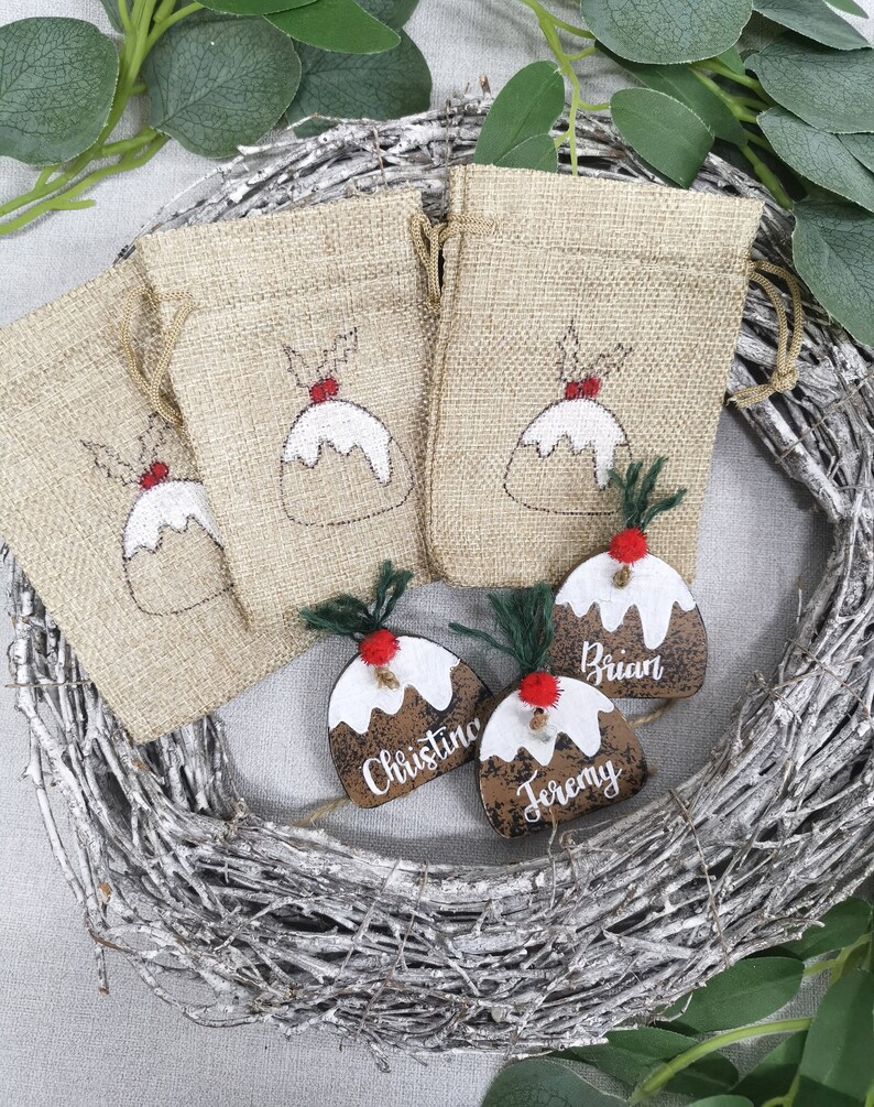 May include: Three brown wooden Christmas ornaments shaped like Christmas pudding with white icing and red holly berries. The ornaments are personalized with the names "Brian", "Christine", and "Jeremy".