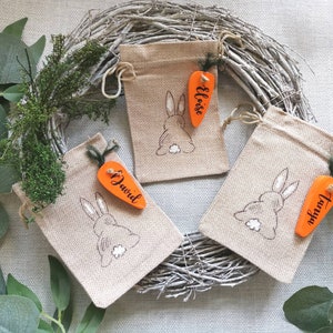 May include: Three small burlap bags with bunny rabbit embroidery and carrot-shaped wooden tags. The tags are personalized with the names "Eloise", "David", and "Taviya".