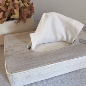 May include: A white wooden tissue box holder with a gray wash finish. The holder has a rectangular shape with a rounded opening for tissues.