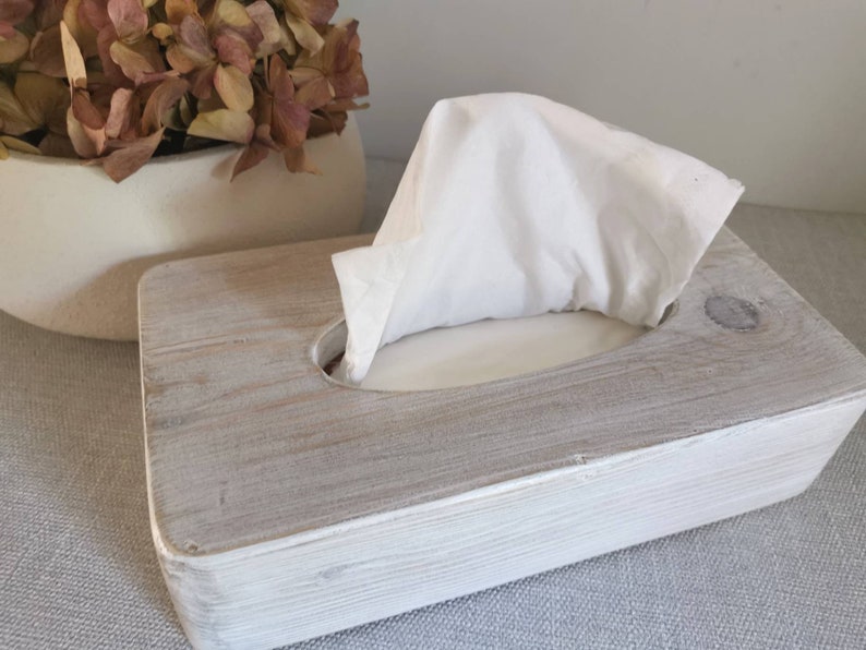 May include: A white wooden tissue box holder with a gray wash finish. The holder has a rectangular shape with a rounded opening for tissues.