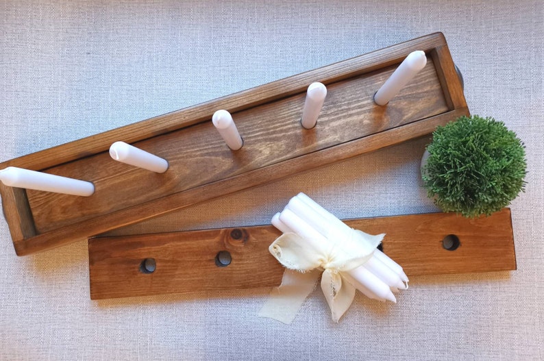 Op de afbeelding: Twee houten kaarsenstandaards, een met vijf gleuven voor kaarsen en de andere met drie gleuven. De standaards zijn in een donkerbruine kleur gebeitst. Een bundel witte kaarsen is vastgebonden met een wit lint.