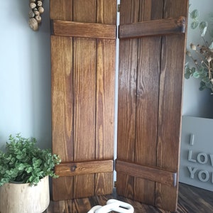 May include: A pair of brown wooden shutters with a distressed finish. The shutters are closed and have a simple design with horizontal slats.