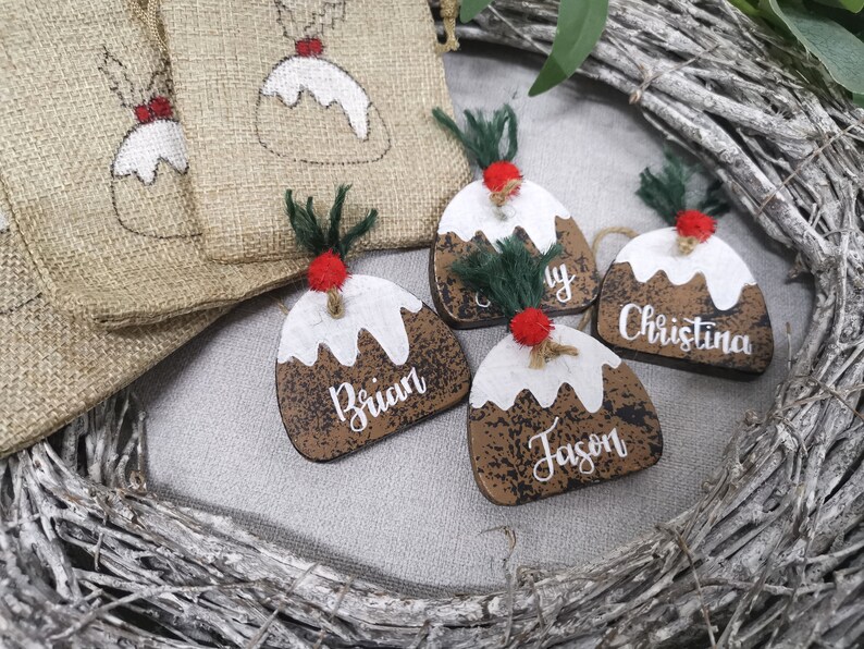 May include: Four wooden Christmas ornaments shaped like Christmas pudding with white icing and brown sauce. Each ornament has a different name written on it: Brian, Jason, Christina, and Amy.
