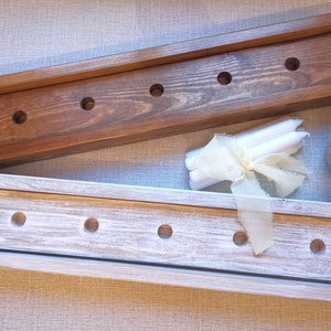 Op de afbeelding: Twee houten kaarsenhouders, een in bruin gebeitst en een in wit geverfd, met gaten voor kaarsen. De houders zijn leeg en er liggen witte kaarsen en een wit lint op de tafel.